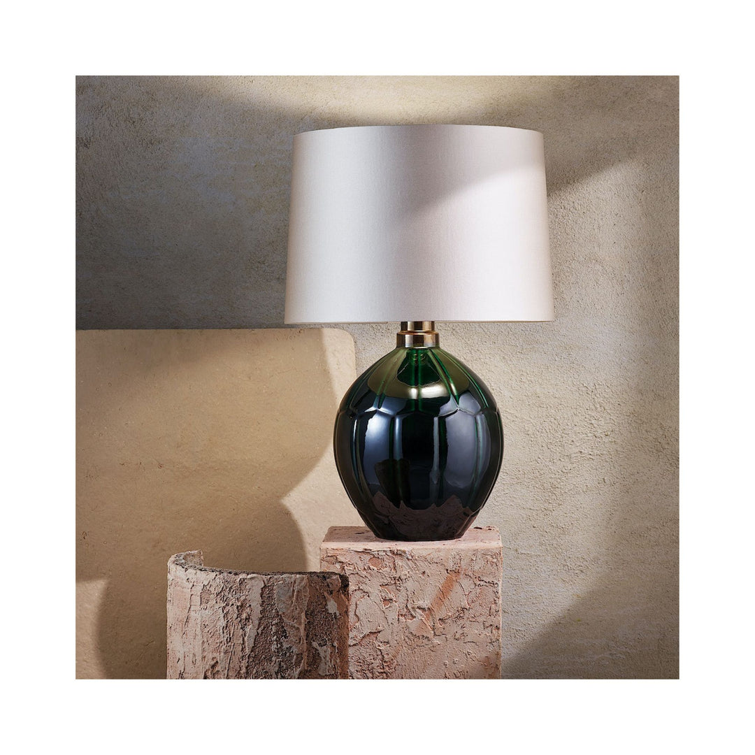 rich emerald green table lamp with cream silk shade on a wood stump with plaster wall behind